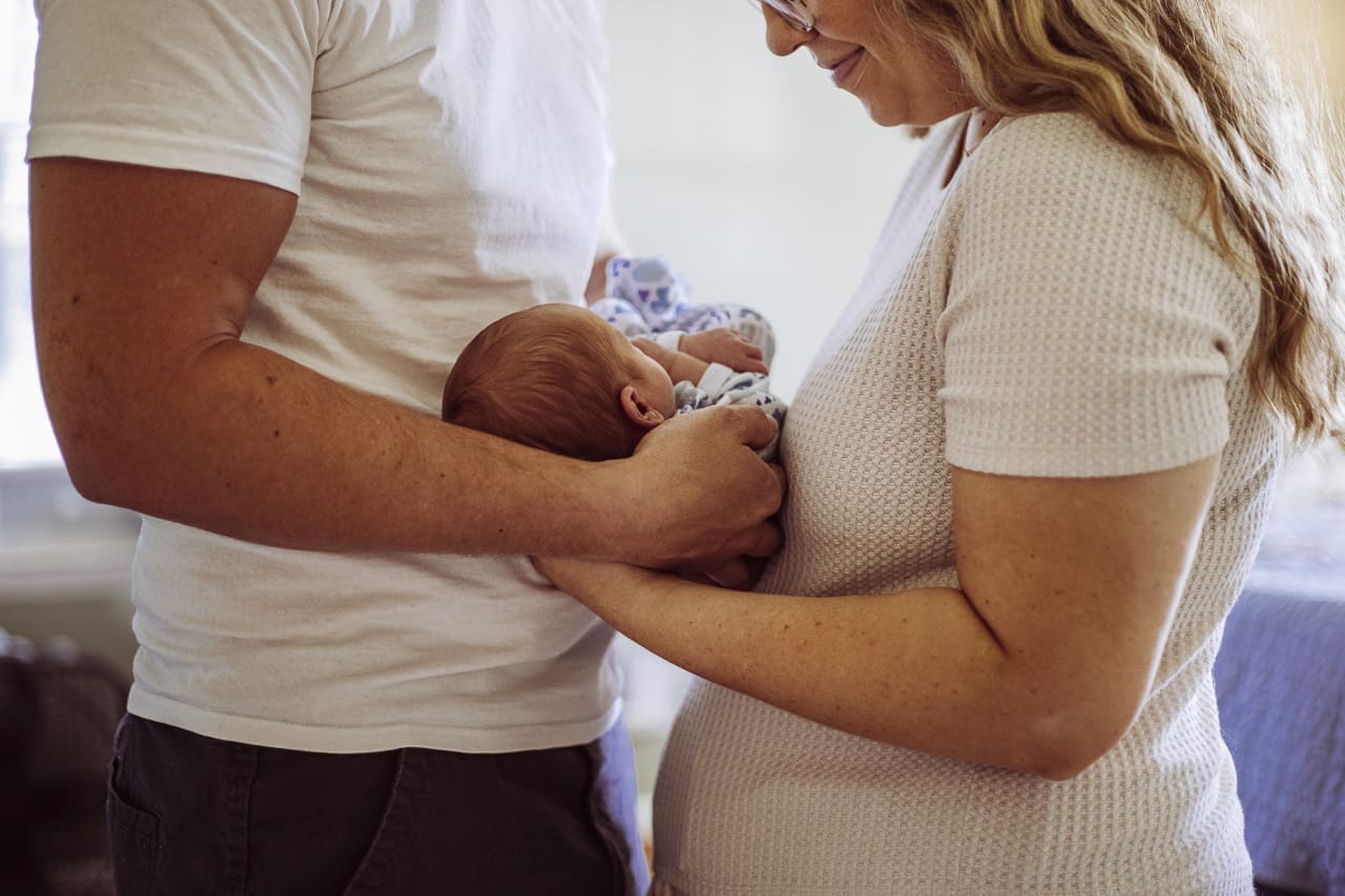 5 stages of pregnancy with Tifton resources: 4th trimester, a Mom and Dad hold their newborn baby between them, looking down lovingly at him
