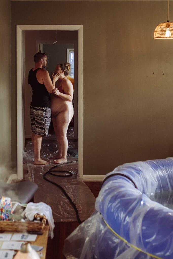5 stages of pregnancy by Tifton birth photographer: birth. Image of laboring woman standing in doorway with her husband cradling her face and speaking supportive words.