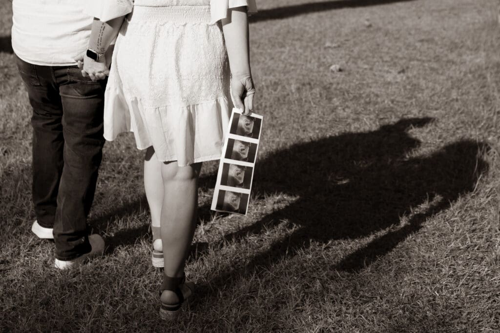 Tifton birth photography: a couple holds hand walking forward, away from the camera, holding their ultrasound behind them as a pregnancy announcement