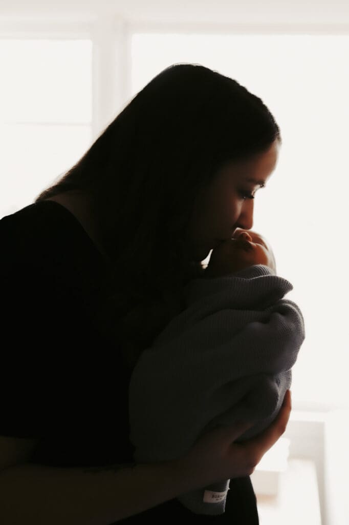 Silhouette of a mother kissing her newborn by Tifton birth photographer