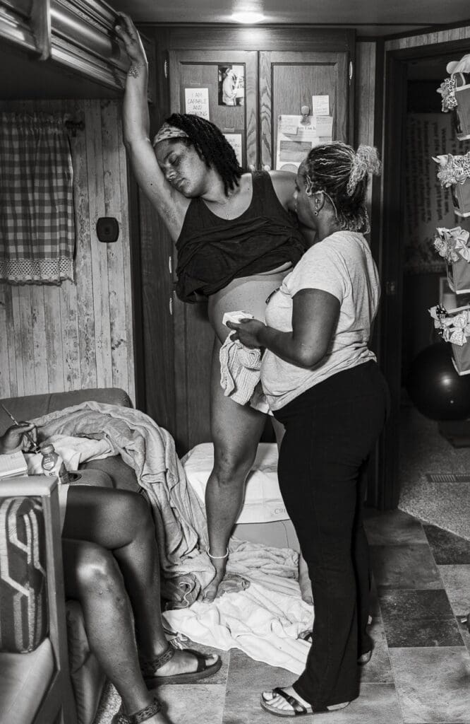 Why birth photography: Image of a woman deeply focused on labor, standing with her hand on the wall while her midwife listens to her belly with a doppler. By Tifton birth photographer