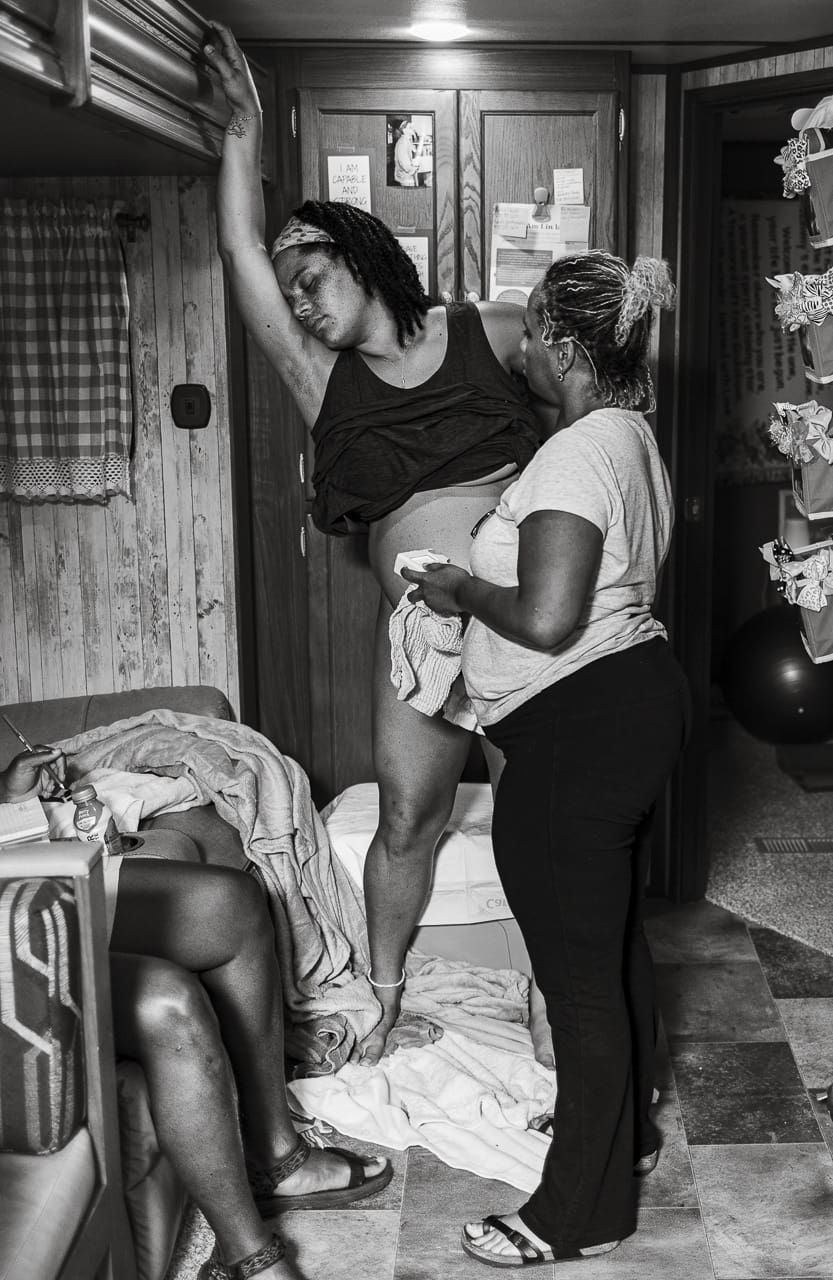 Why birth photography: Image of a woman deeply focused on labor, standing with her hand on the wall while her midwife listens to her belly with a doppler. By Tifton birth photographer
