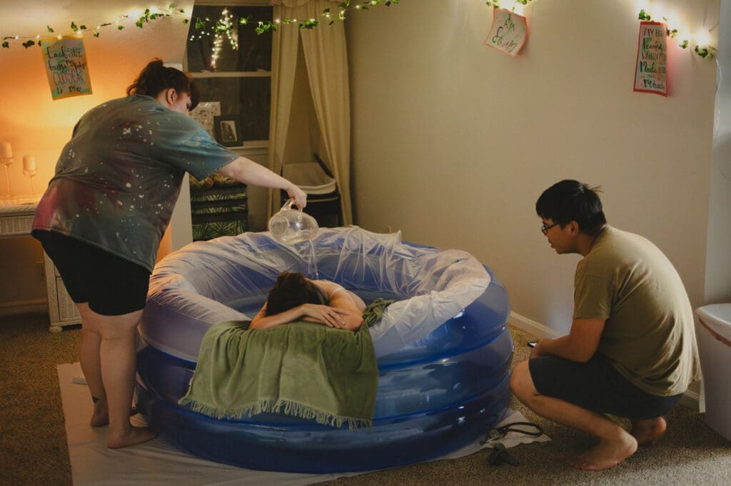 Laboring mother in the birth pool,  supported by sister and partner, creating a positive birth experience by Tifton birth photographer
