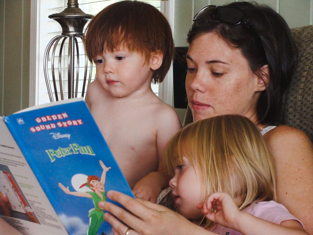 Finding balance in motherhood: a mother sits with two children in her lap, reading a book together, by Tifton photographer