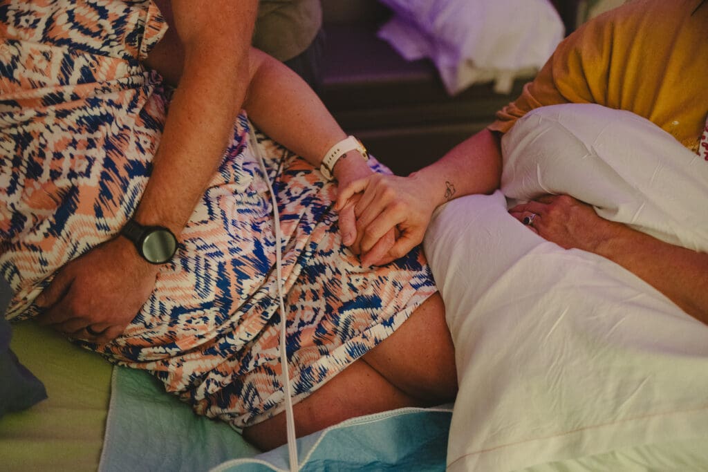 Doula providing emotional support in Tifton, GA: a husband has his arm around pregnant wife's belly while a doula sits nearby and holds her hand for emotional support