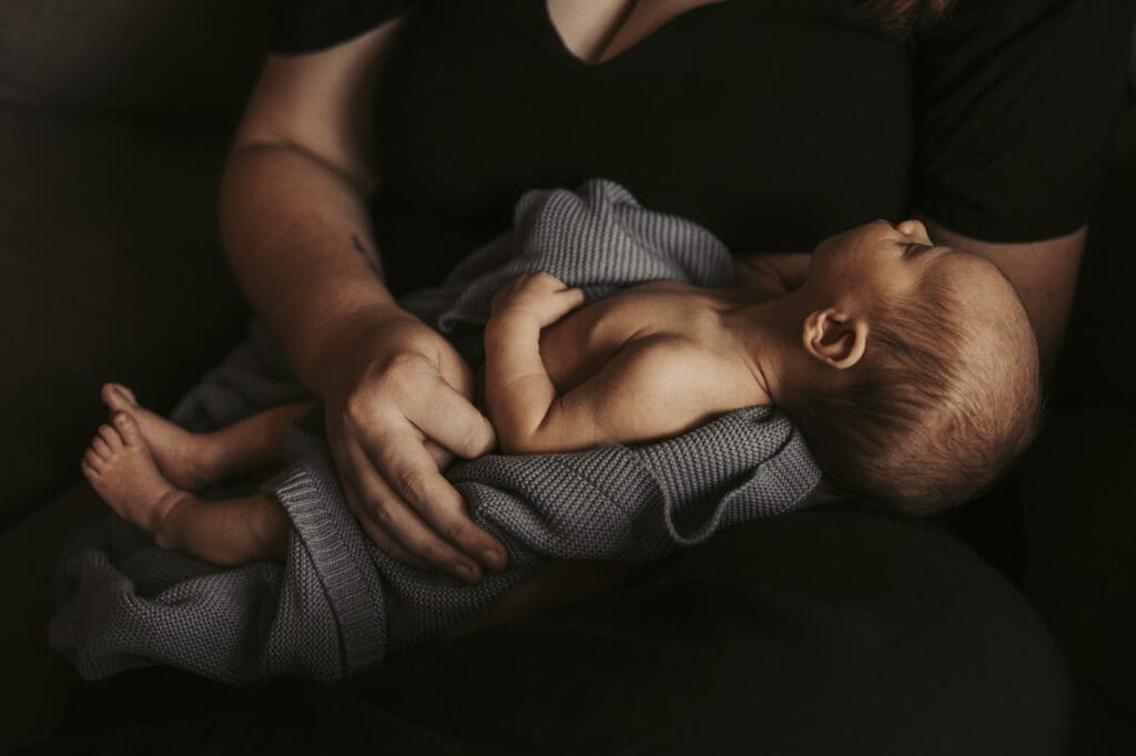 Mother holding newborn swaddled in a soft blanket during early postpartum recovery by Tifton birth and lifestyle newborn photographer