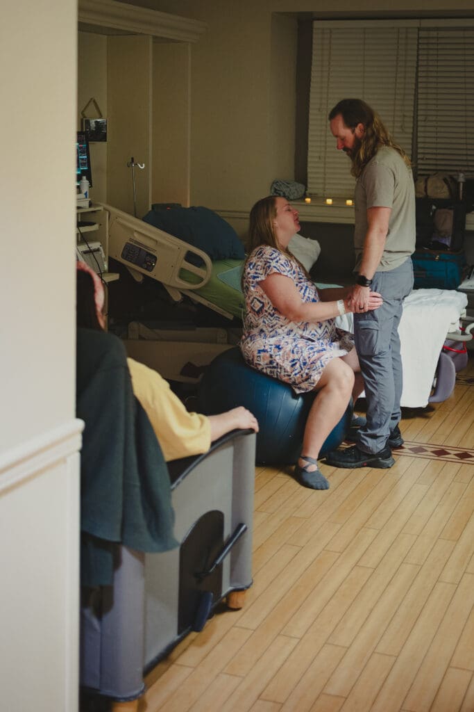 A doula sits quietly aside in a peaceful moment during labor while a husband supports his wife